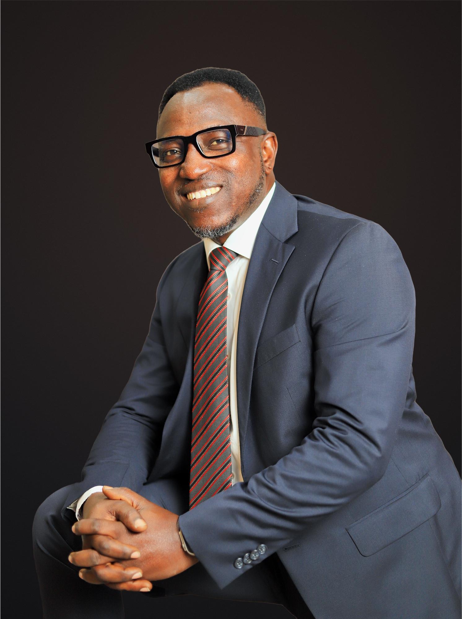 Dr. Sunday Olorunsheyi seated, leaning forward with hands clasped