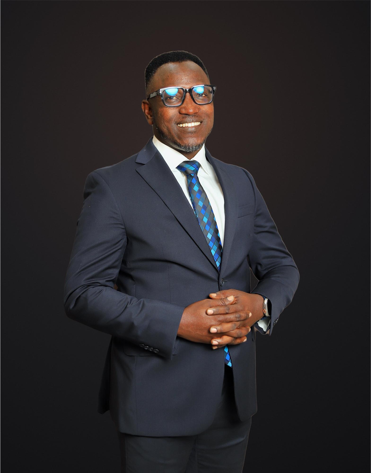 Dr. Sunday Olorunsheyi in a dark suit and blue tie, hands clasped